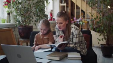 The girl is studying with a tutor. The child writes in a notebook, the literature teacher dictates the task. Textbooks and a laptop are on the table. High quality 4k footage