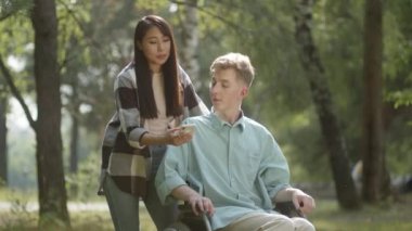 Being in the public park in a good weather, a young sweet couple decide calling their friends, they wave hands and smile. High quality 4k footage