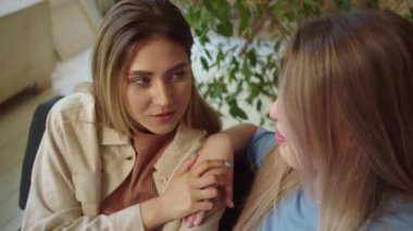 Two handsome women are sitting in the living room on the sofa, talking to each other and sharing their problems. High quality FullHD footage