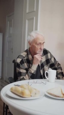 A young woman and her grandfather with a beard sit at the table and have tea. On the table are fruits and pastries. They communicate on serious and vital topics