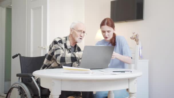 老人と女性が居間のテーブルに腰を下ろしている 彼らはオンラインで税金を支払うためにラップトップを使用します 高品質4K映像 — ストック動画