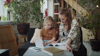 A woman does her daughter school lessons. They are sitting at the table with textbook. High quality 4k footage
