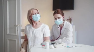 Bir doktor steteskoplu yaşlı bir kadının akciğerlerini dinler. Hademe hastanın kalp atışlarını dinlemek için arkasını dönmesini istiyor. Yüksek kalite 4k görüntü