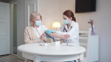 Önlüklü ve tıbbi maskeli bir kadın hastaların kan basıncını ölçer. Doktor bir tonometre kullanır. Yüksek kalite 4k görüntü