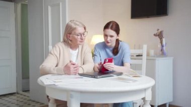 Yaşlı bir kadın cep telefonunu nasıl kullanacağını açıklayan kızı dinliyor. Soruları faiziyle soruyor. Yüksek kalite 4k görüntü