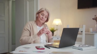 Yaşlı bir kadın bir kutu kablosuz kulaklık açıyor. Kulaklarına takıyor ve bilgisayardan müzik çalıyor. Yüksek kalite 4k görüntü