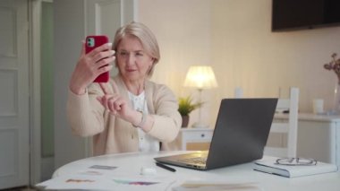 Emeklinin biri büyük bir yemek odasında oturur ve akıllı telefondan selfie çeker. Ciddi görünüyor. Yüksek kalite 4k görüntü