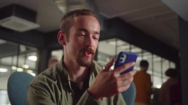 Genç bir erkek öğrenci sandalyede oturur ve video konuşmasında arkadaşlarıyla konuşur, kapat. Yüksek kaliteli FullHD görüntüler