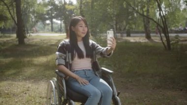 Kamu parkında tekerlekli sandalyede oturan uzun siyah saçlı, oldukça engelli Asyalı bir kız arkadaşıyla FaceTime 'da konuşmayı kesiyor. Yüksek kalite 4k görüntü
