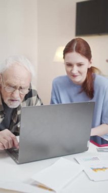 Gözlüklü bir adam masada tekerlekli sandalyede oturuyor. Önünde bir dizüstü bilgisayar var. Tuşlara basıp arama sorguları yazmaya çalışıyor. Genç bir kadın ona yardım ediyor. Yüksek kalite 4k görüntü