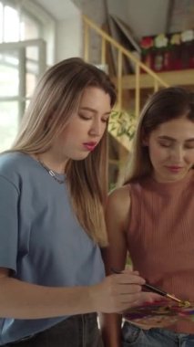 İki sevimli kız arkadaş stüdyoda duruyorlar, gülümsüyorlar ve birlikte resim çiziyorlar. Yüksek kaliteli FullHD görüntüler