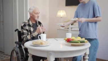 Bir kadın yemek odasına girer ve masaya tabaklar dolusu sandviç koyar. Oturdu ve gözlüklü yaşlı bir adamla konuşmaya başladı. Yemekleri tartışıyorlar. Yüksek kalite 4k görüntü