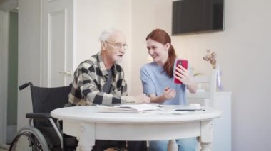 Bir kadın kendi ve tekerlekli sandalyedeki bir adamın telefonda fotoğrafını çekiyor. Sonuçlara bakıp gülümsüyorlar. Yüksek kalite 4k görüntü
