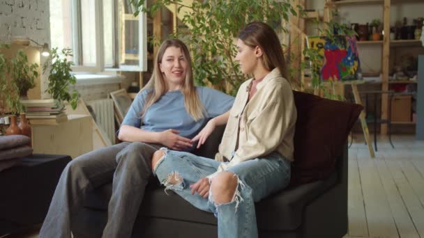 Дві Красиві Дівчата Сидять Вітальні Дивані Розмовляючи Один Одним Тримаючись — стокове відео