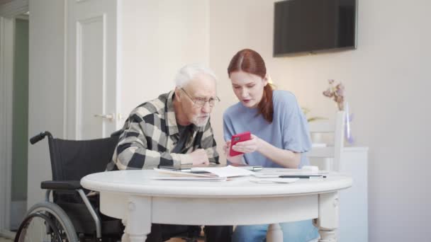 Pensionista Aprendendo Usar Smartphone Senta Mesa Numa Cadeira Rodas Ouve — Vídeo de Stock