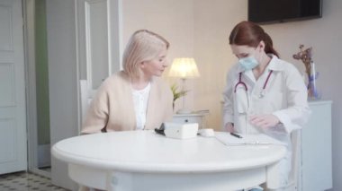 Hemşire hastaların evine gelir. Doktor hastanın yanına oturur ve bir tıbbi maske takmak ister. Yüksek kalite 4k görüntü