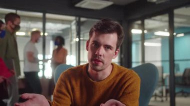 Genç bir erkek öğrenci üniversitede sandalyede oturuyor ve kameraya konuşuyor, kapatın. Yüksek kalite 4k görüntü