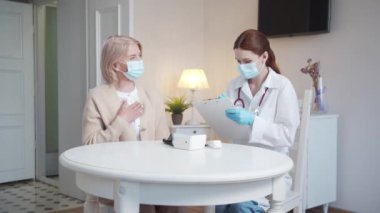 Yaşlı bir kadın doktorların sorularını cevaplar. Hademe tablete not alır. Oturma odasında oturuyorlar. Yüksek kalite 4k görüntü