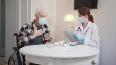 Tekerlekli sandalyedeki yaşlı bir adam sağlık sorunları hakkında doktora şikayette bulunuyor. Tablete notlar yazıyor. Yüksek kalite 4k görüntü