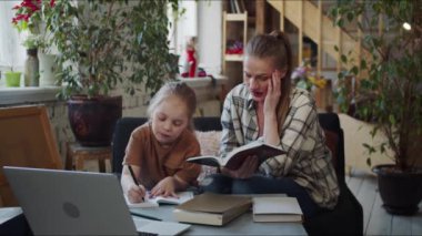 Bir anne kızına bir kitaptan bir mesaj okur. Çocuk bir okul defterine yazıyor. Kadın yorgun ve bitkin görünüyor. Kızı ödev yapmaya devam etmesini istiyor. Yüksek kalite 4k görüntü