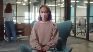 Uzun saçlı genç bir öğrenci kız koruyucu yüz maskesini çıkarıyor ve gülümseyen kameraya bakıyor. Yüksek kalite 4k görüntü