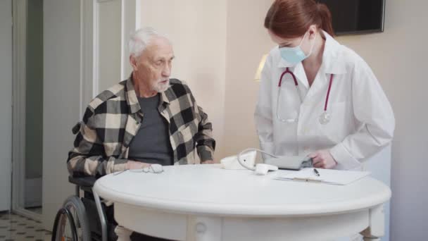 女医が部屋に入り 車椅子の老人の隣に座る 彼女は医療用手袋を装着し 検査の準備をする 高品質4K映像 — ストック動画