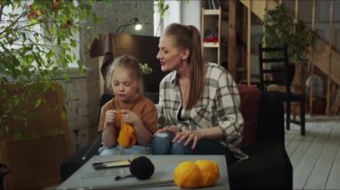 Bir kadın küçük bir çocukla kanepede oturuyor. Bir kıza atkı örmeyi öğretiyor. Yüksek kalite 4k görüntü