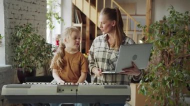 Bir kadın dizüstü bilgisayar tutuyor ve bir kız da bir sentezleyicinin yanında duruyor. Annem müzik öğretmenini çağırıyor ve ders başlıyor. Yüksek kalite 4k görüntü