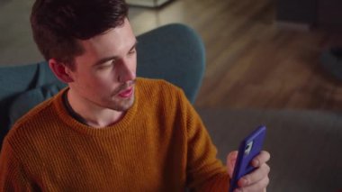Genç bir erkek öğrenci sandalyede oturur ve video konuşmasında arkadaşlarıyla konuşur, kapat. Yüksek kaliteli FullHD görüntüler