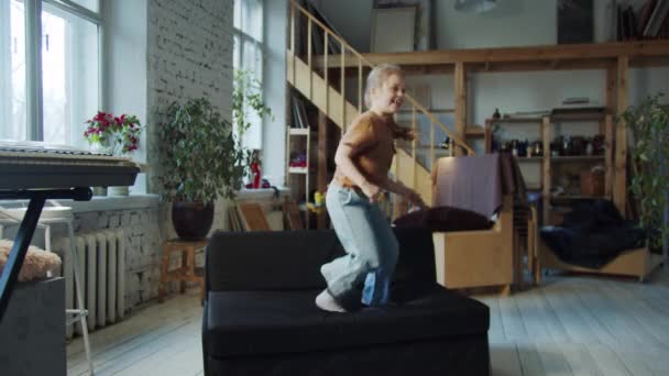Das Kind Springt Freudig Auf Das Schwarze Sofa Während Die — Stockvideo