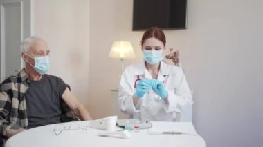 Bir kadın hastasına koronavirüse karşı aşı seçmesini öneriyor. Tekerlekli sandalyedeki bir adam bir seçim yapar. Doktor bir şırınga ile paketi açar ve aşı için hazırlanır. Yüksek kalite 4k