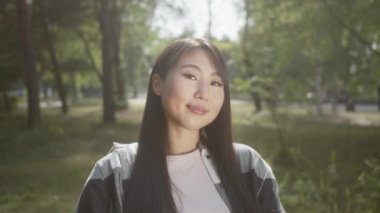 Uzun saçlı Asyalı bir kadın halka açık bir parkta tekerlekli sandalyede oturuyor, gülümsüyor ve saçlarına dokunuyor. Yüksek kalite 4k görüntü