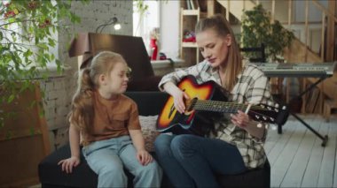 Kız gitar çalan müzik öğretmenine sabırsızlıkla bakıyor. Çocuk kadının gitarını alır ve çalmaya çalışır.