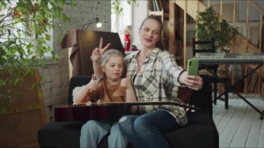 Bir kadın kendi ve kızının akıllı telefonuyla fotoğrafını çeker. Birbirlerine boynuz takıp gitarı gösteriyorlar. Telefon ekranına bakıyorlar ve fotoğrafları değerlendiriyorlar. Eğleniyorlar.