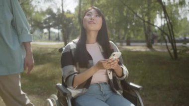 Genç engelli bir kız telefonda bir şey izliyor ve en iyi arkadaşıyla parkta buluşuyor. Yüksek kaliteli FullHD görüntüler