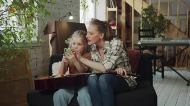 Bir kadın ve çocuğu kanepede oturuyorlar. Kız internete düştü. Annem onu izliyor ve onunla dalga geçiyor. Yüksek kalite 4k görüntü