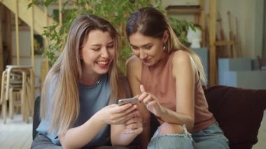 İki güzel Igbt kızı kanepede oturup telefonda komik videolar izliyorlar. Yüksek kaliteli FullHD görüntüler