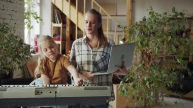 Bir kadın bir sentezleyicinin yanında duruyor ve dizüstü bilgisayardaki notlara bakıyor. Tavsiye verir ve kıza öğretir. Yüksek kalite 4k görüntü