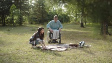 Yakışıklı genç Asyalı bir kız halka açık bir parkta yere ekose çizer ve engelli erkek arkadaşının tekerlekli sandalyeden inmesine yardım eder. Yüksek kalite 4k görüntü