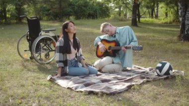 Kamu parkında güzel bir havada, iki en iyi arkadaş ekose üzerinde oturuyor, engelli genç bir adam gitar çalıyor ve uzun saçlı Asyalı güzel bir bayan şarkı söylüyor ve alkışlıyor.
