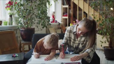 Bir anne ve çocuğu geniş bir çatı katında bir kanepede oturuyorlar. Annem bir kağıt parçası çıkardı ve kızıyla birlikte kalemlerle çizmeye başladı. Yüksek kalite 4k görüntü