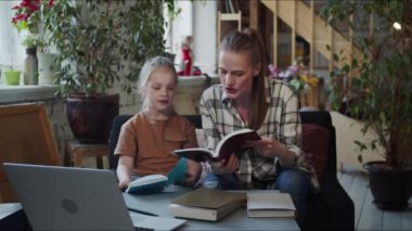 Kadın ve kızı okula hazırlanmak için dizüstü bilgisayar ve ders kitapları kullanıyorlar.