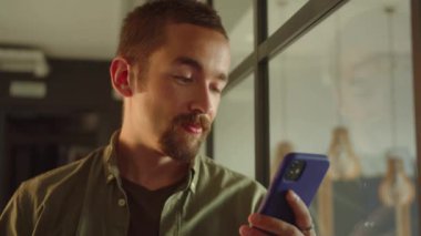 Genç bir erkek öğrenci pencerenin yanında duruyor, internette yazılar okuyor ve sonra kameraya bakıp gülümsüyor.