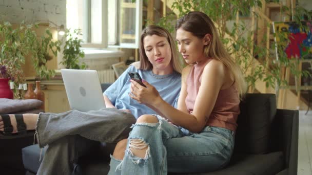Két fiatal, gyönyörű hölgy keres az interneten a laptopon, beszélgetnek és mosolyognak. — Stock videók