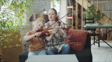 Öğretmen kızın keman çalmasına yardım eder ve yayı ayarlar.