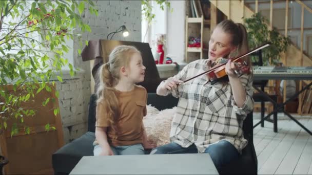 Mamá toca el violín delante de su hija. Hija se ríe y sacude la cabeza — Vídeo de stock