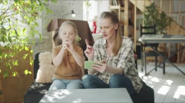 Anne, kızına telefonda bir video izleterek flüt çalmasını öğretiyor.