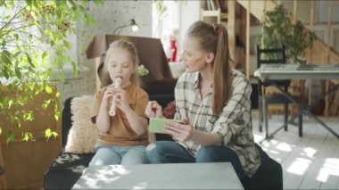 Bir kız ve genç annesi telefonda flüt dersleri izliyorlar. Hobisi olan bir çocuğa yardım etmeye çalışan bir kadın.