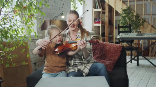 Женщина держит ребенка за руку с луком и помогает играть на скрипке — стоковое видео