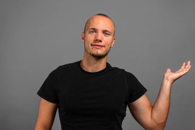 Gülümseyen genç, gri bir arka planda avucunda bir şey sunuyor.